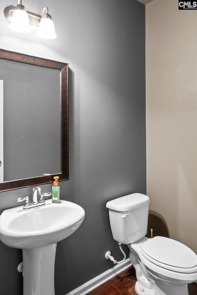 half bathroom with toilet, a sink, baseboards, and wood finished floors