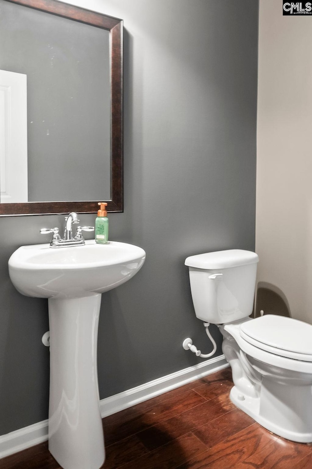 half bath featuring toilet, a sink, baseboards, and wood finished floors