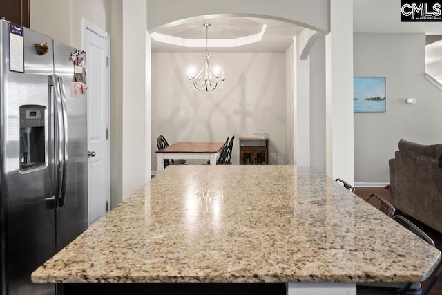 kitchen with arched walkways, a raised ceiling, light stone counters, and stainless steel fridge