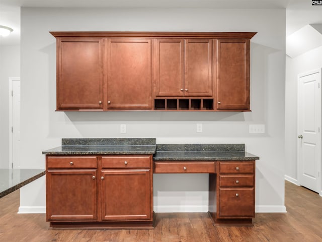 kitchen with baseboards, dark wood finished floors, dark stone countertops, and built in study area