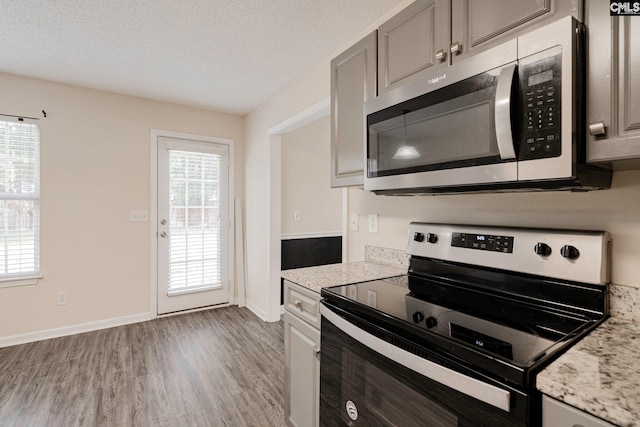 kitchen with a textured ceiling, stainless steel appliances, light wood-type flooring, and plenty of natural light