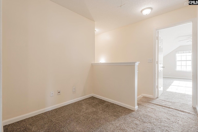 spare room featuring lofted ceiling, a textured ceiling, carpet, and baseboards