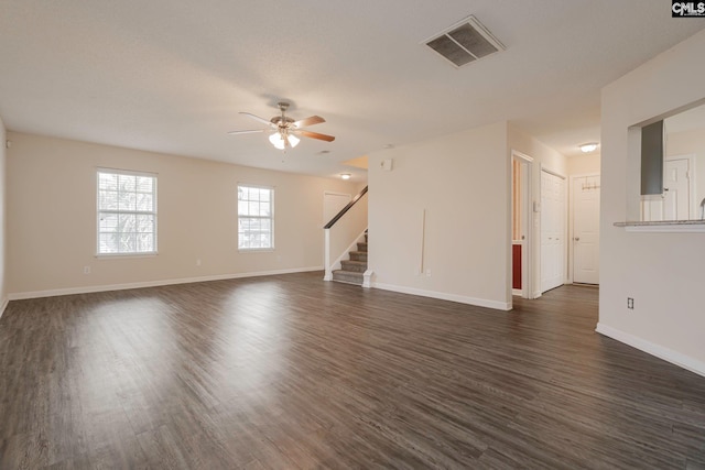 unfurnished room featuring ceiling fan, visible vents, baseboards, stairs, and dark wood-style floors