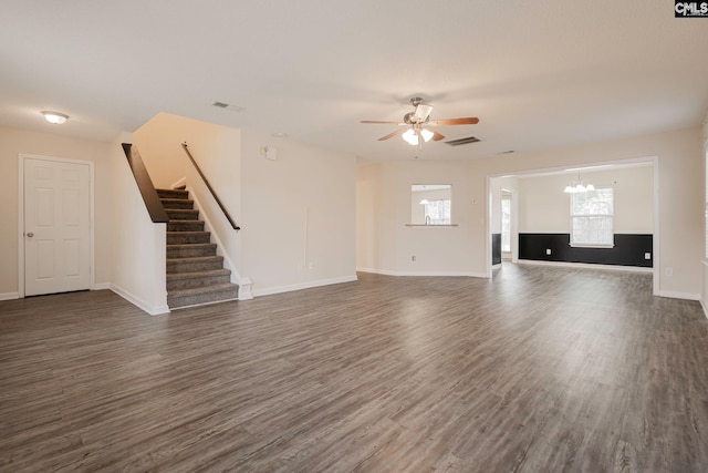 unfurnished living room featuring ceiling fan with notable chandelier, visible vents, dark wood finished floors, and stairs