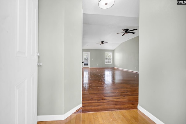 interior space with ceiling fan, vaulted ceiling, wood finished floors, and baseboards