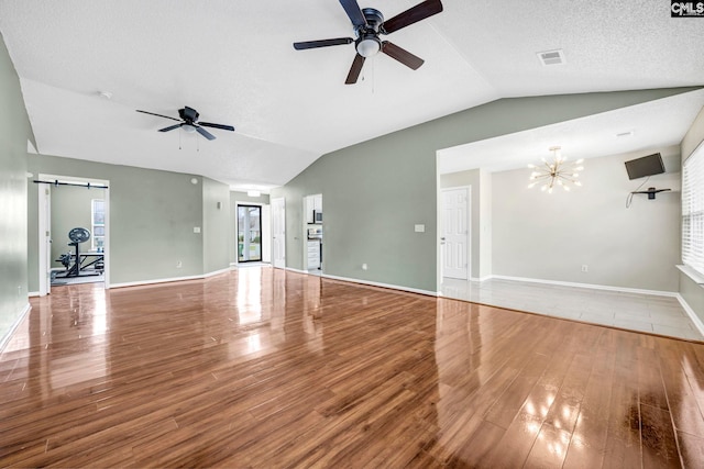 unfurnished living room featuring lofted ceiling, a barn door, wood finished floors, and visible vents