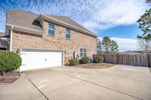 view of side of property with brick siding, fence, concrete driveway, roof with shingles, and a gate