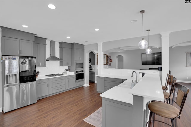 kitchen with a breakfast bar, wall chimney range hood, stainless steel appliances, and gray cabinetry