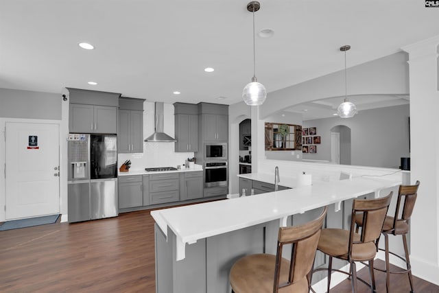 kitchen featuring gray cabinetry, stainless steel appliances, decorative backsplash, wall chimney exhaust hood, and dark wood finished floors