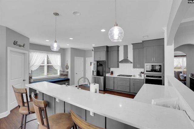 kitchen featuring arched walkways, decorative backsplash, wall chimney exhaust hood, appliances with stainless steel finishes, and gray cabinetry