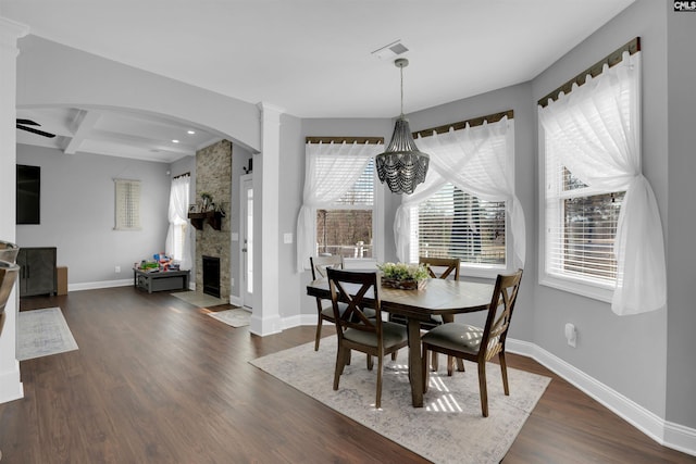 dining room with visible vents, dark wood-type flooring, a stone fireplace, coffered ceiling, and baseboards