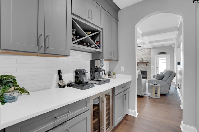 kitchen with arched walkways, a fireplace, gray cabinetry, dark wood-type flooring, and coffered ceiling