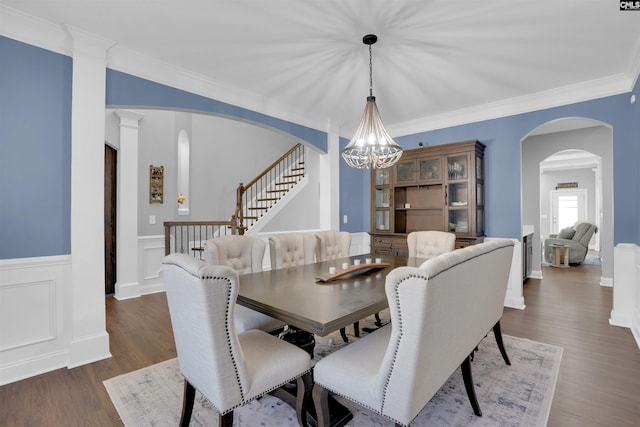 dining room with arched walkways, crown molding, wood finished floors, stairs, and an inviting chandelier