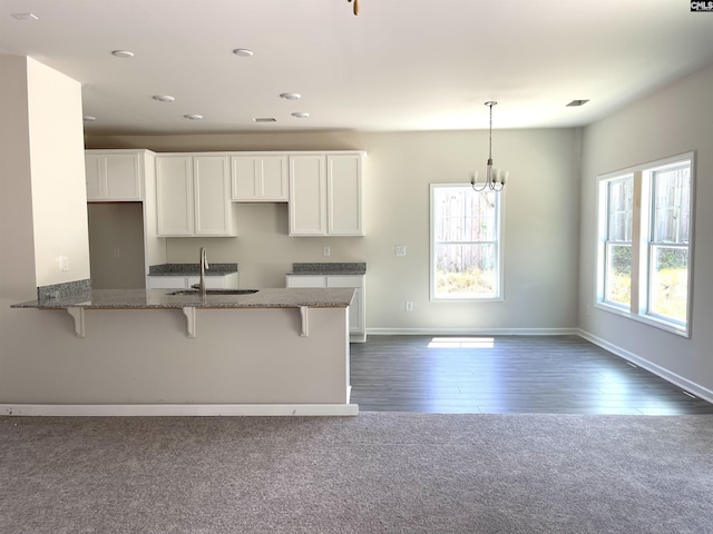 kitchen featuring stone counters, a breakfast bar, a sink, white cabinetry, and baseboards