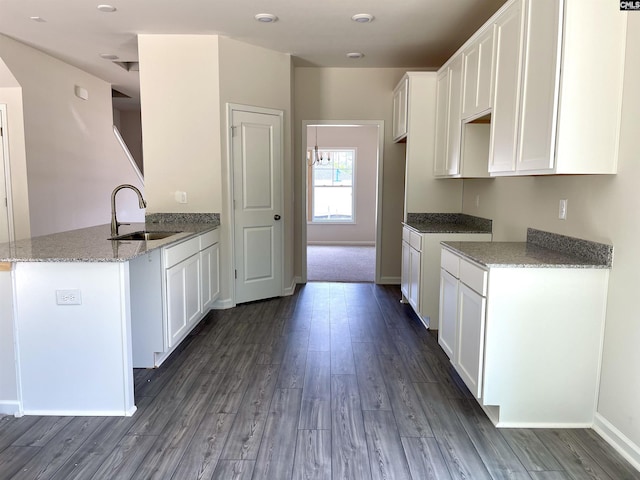 kitchen featuring light stone counters, dark wood finished floors, white cabinets, a sink, and a peninsula