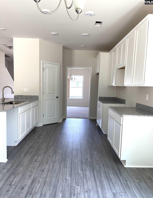kitchen with visible vents, white cabinets, light stone counters, wood finished floors, and a sink