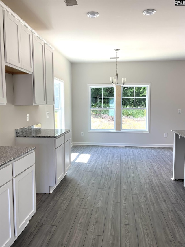 kitchen with stone countertops, white cabinets, dark wood finished floors, and an inviting chandelier