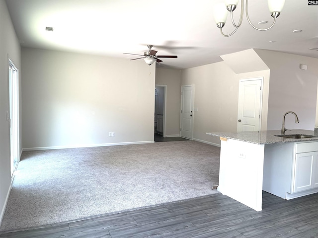 kitchen featuring ceiling fan, light stone counters, a sink, white cabinetry, and carpet