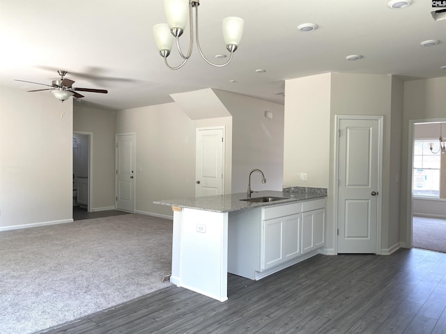 kitchen featuring open floor plan, white cabinets, a sink, light stone countertops, and a peninsula