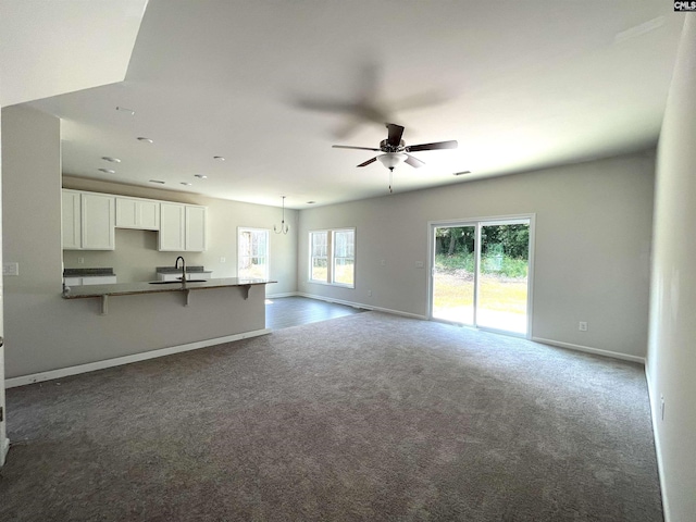 unfurnished living room with baseboards, dark carpet, a sink, and ceiling fan
