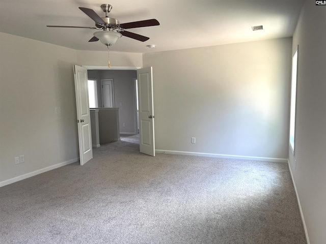 spare room with a ceiling fan, a wealth of natural light, light colored carpet, and baseboards