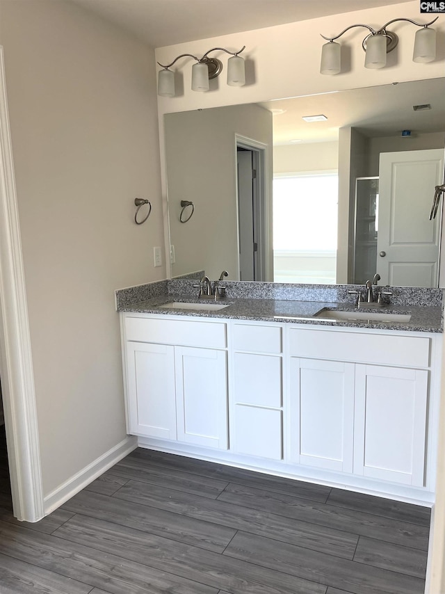 bathroom with a stall shower, double vanity, a sink, and wood finished floors