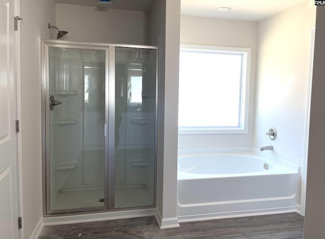 full bath with a stall shower, wood finished floors, a bath, and baseboards