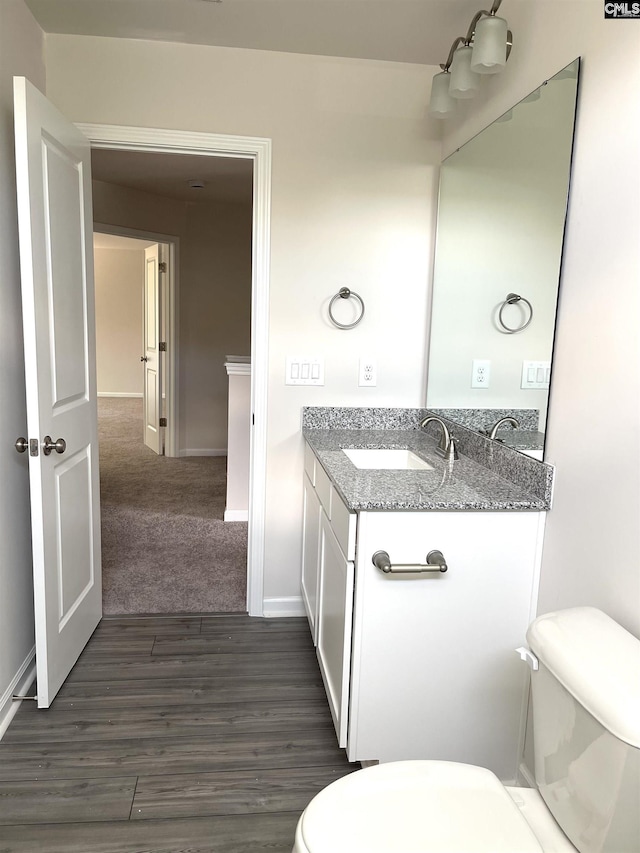 half bathroom featuring toilet, baseboards, wood finished floors, and vanity