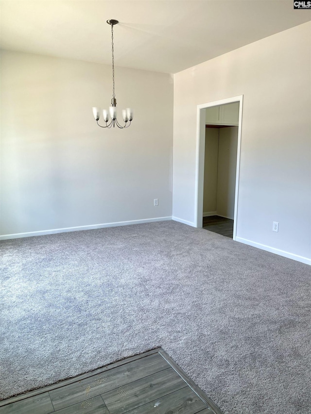 unfurnished room with baseboards, dark colored carpet, and an inviting chandelier