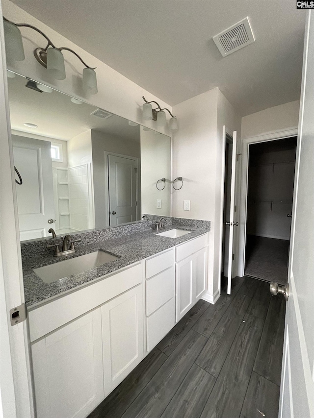 full bath with double vanity, visible vents, a sink, and wood finished floors