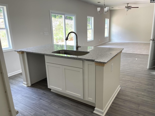 kitchen featuring a sink, open floor plan, light stone countertops, an island with sink, and pendant lighting