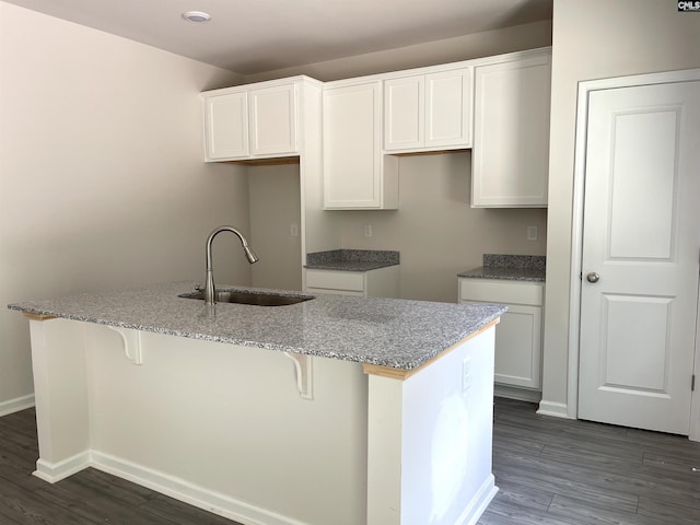 kitchen with a center island with sink, dark wood-style floors, a breakfast bar, white cabinetry, and a sink