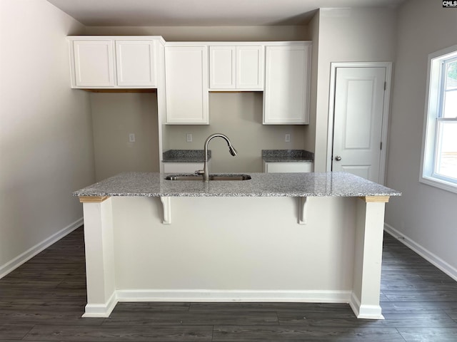 kitchen featuring dark wood-style floors, a kitchen island with sink, white cabinetry, a sink, and baseboards