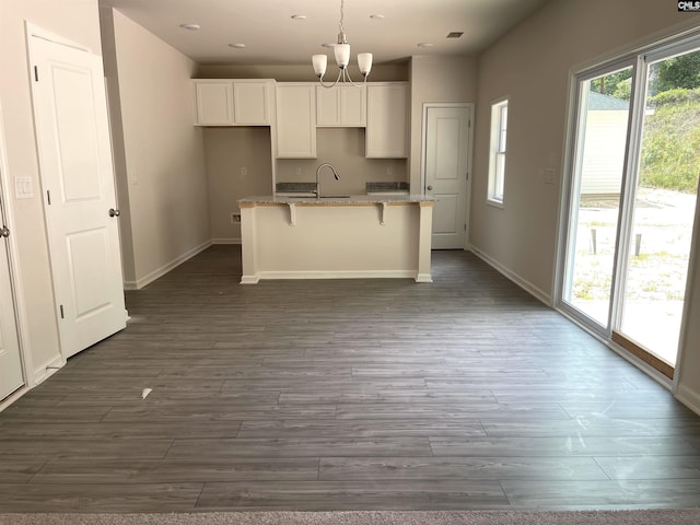 kitchen with a kitchen island with sink, a sink, white cabinetry, baseboards, and dark wood finished floors