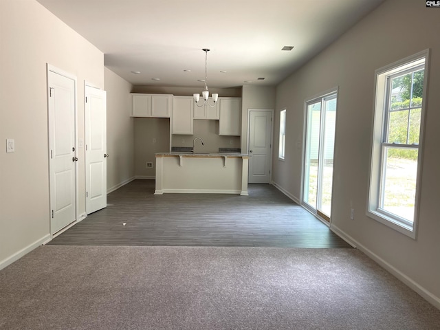 kitchen featuring a sink, white cabinets, baseboards, a center island with sink, and an inviting chandelier