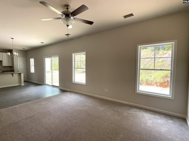 unfurnished living room with dark carpet, baseboards, and ceiling fan with notable chandelier