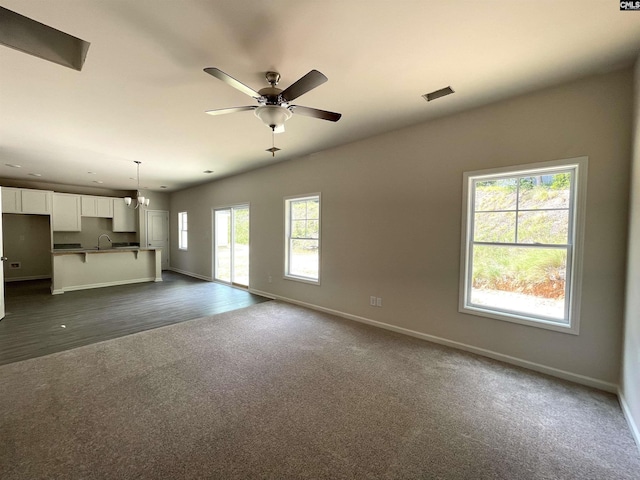 unfurnished living room with a ceiling fan, dark colored carpet, visible vents, and baseboards