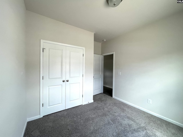 unfurnished bedroom with baseboards, dark carpet, and a closet