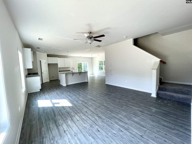 unfurnished living room featuring dark wood finished floors, ceiling fan, a sink, baseboards, and stairs