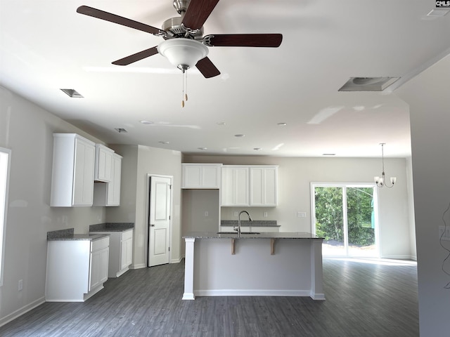 kitchen with dark wood finished floors, white cabinets, a sink, an island with sink, and baseboards