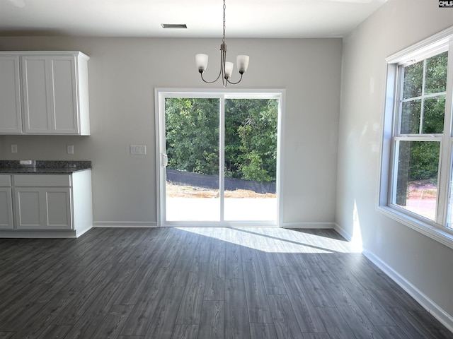 unfurnished dining area with dark wood-type flooring, visible vents, baseboards, and an inviting chandelier