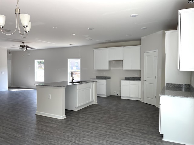 kitchen featuring dark wood-style flooring, white cabinetry, a sink, and a center island with sink