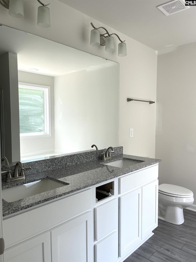 bathroom featuring toilet, double vanity, a sink, and visible vents