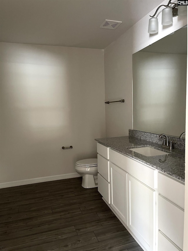 half bath with baseboards, visible vents, toilet, wood finished floors, and vanity