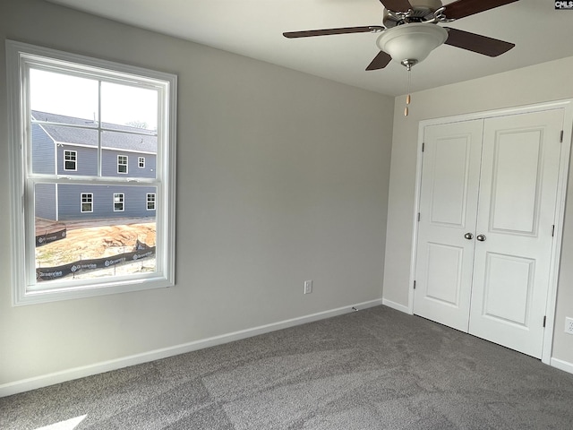 unfurnished bedroom with a closet, dark carpet, a ceiling fan, and baseboards