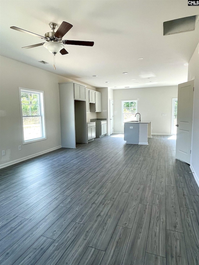 unfurnished living room featuring dark wood-style floors, ceiling fan, visible vents, and baseboards