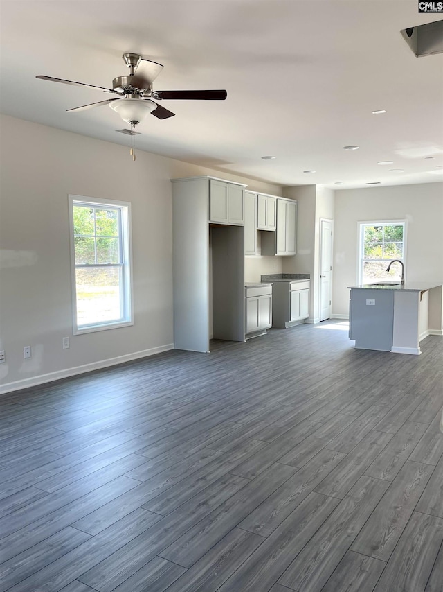 unfurnished living room featuring dark wood-style floors, a healthy amount of sunlight, a sink, and baseboards