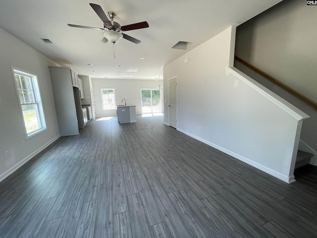 unfurnished living room with stairway, ceiling fan, visible vents, and dark wood finished floors