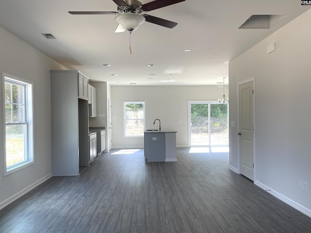 kitchen featuring dark wood-style flooring, a center island with sink, and baseboards