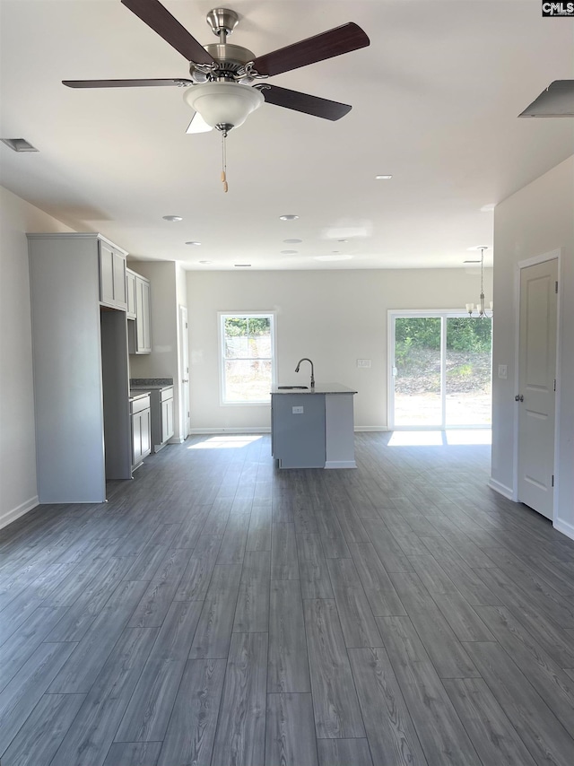 unfurnished living room with a sink, a ceiling fan, visible vents, baseboards, and dark wood finished floors